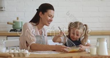 快乐的30岁的母亲看着学龄前的小女儿搅拌鸡蛋。